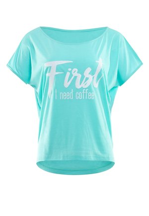 T-shirt corto azzurro chiaro a maniche corte, dalla vestibilità rilassata, con testo bianco "Prima ho bisogno di caffè" in un mix di caratteri corsivi e stampatello.