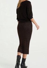 Mörkbrun midiklänning med en figursydd silhuett, stickad textur och korta ärmar. Bärs med svarta högklackade stövlar.