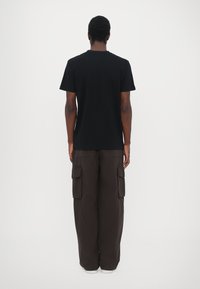 Tricou negru cu mânecă scurtă și guler rotund, asortat cu pantaloni cargo maro închis, cu mai multe buzunare și o croială lejeră.