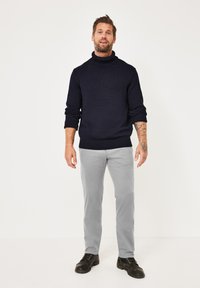 Navy knitted turtleneck sweater paired with light gray slim-fit pants and black lace-up boots. Smooth texture and casual design.