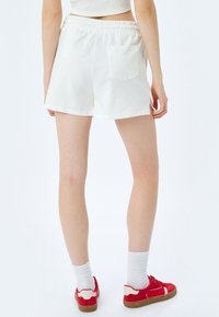 Witte katoenen shorts met een elastische tailleband, zijzakken en een achterzak. Draag met rode sneakers en witte sokken.