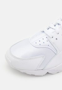 Scarpa atletica bianca caratterizzata da una combinazione di pelle liscia e tessuto testurizzato, con sezioni perforate, lacci standard e una suola imbottita.