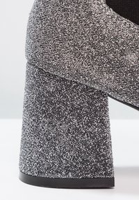 Chaussure à talon haut épais avec un tissu texturé noir et blanc tacheté couvrant le talon et la partie supérieure.