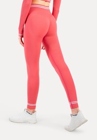 Jaskrawo różowe legginsy z wysokim stanem, z białymi paskami na mankietach, gładką teksturą i dopasowanym krojem.