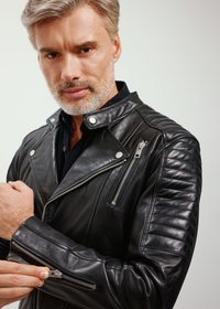 Czarna skórzana kurtka motocyklowa z srebrnymi zamkami, charakterystycznym kołnierzem, pikowanymi detalami na ramionach oraz teksturowanym wykończeniem.
