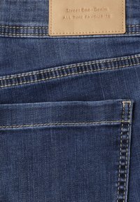 Achterzak van spijkerbroek met beige leren label met de tekst "Street One - Denim ALL TIME FAVOURITE", dubbel gestikte naden in blauwe stof.