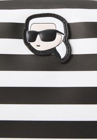 Un material a rayas en blanco y negro presenta un parche de estilo caricaturesco con una cara que lleva gafas de sol, añadiendo un elemento de diseño divertido.