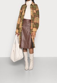 Brązowa, pomarańczowa i zielona koszula-jesionka w kratkę; dopasowana brązowa skórzana spódnica; biała bluzka z golfem; beżowe wysokie kozaki; biała torba na ramię.