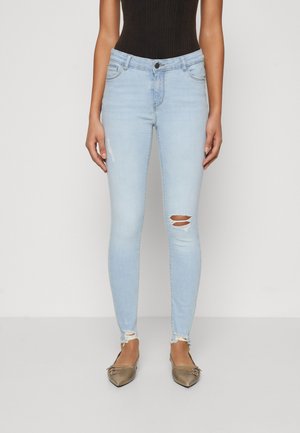 Light blue skinny jeans with ripped knee details and frayed hems, made of denim. Worn with pointed-toe flats in a metallic finish.