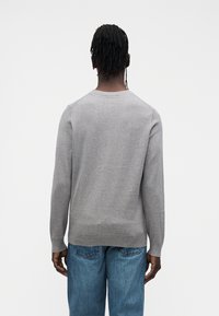 Šedý svetr s dlouhými rukávy, kulatým výstřihem, hladkou texturou a přiléhavým lemem, kombinovaný s světle modrými džínami.