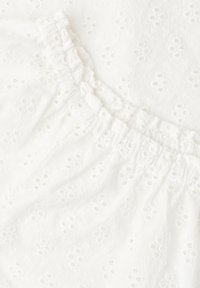 Tissu blanc avec petits motifs de fleurs brodées en œillet et détail de taille élastiquée froncée.
