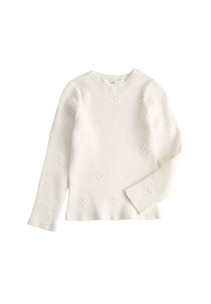 Smilende barn iført en hvid tekstureret sweater og blå jeans med "kindness" broderet på lommen, poserer foran en ensfarvet baggrund.