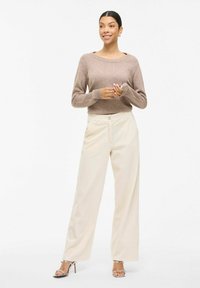Beige stickad tröja med vid halsringning, tillsammans med krämfärgade vida corduroybyxor. Modellen bär silverfärgade klacksandaler.