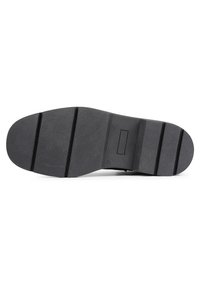 Suela de zapato de goma negra con una superficie lisa, tres ranuras horizontales y un detalle de logo en relieve rectangular.