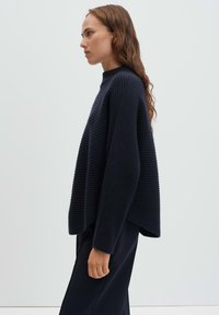 Maglione a costine blu navy con collo alto e spalle scese, caratterizzato da una vestibilità ampia e tessuto strutturato. Design semplice senza motivi.