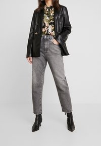 Blazer de cuero negro, camisa de flores de manga corta, vaqueros grises de tiro alto y botines negros de punta. Atuendo simple y casual con texturas contrastantes.