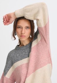 Maglione lavorato a maglia con blocchi di colore orizzontali in grigio, rosa e crema. Collo a coste e maniche larghe. Tessuto morbido e testurizzato.