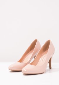 Nude lackläder högklackade skor med rundade tår och en stiletthäl på 8,9 cm, som har en slät yta och en minimalistisk design.