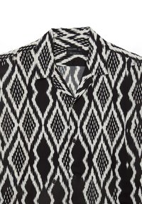 Chemise à manches courtes noire et blanche avec un motif en losanges, coupe décontractée et fermeture par bouton. Fabriquée en tissu léger.