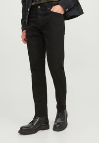 Jeans negros de corte ajustado, fabricados con un denim resistente. Presentan bolsillos laterales, presillas para cinturón y una textura suave. Combinados con botas negras de cordones.