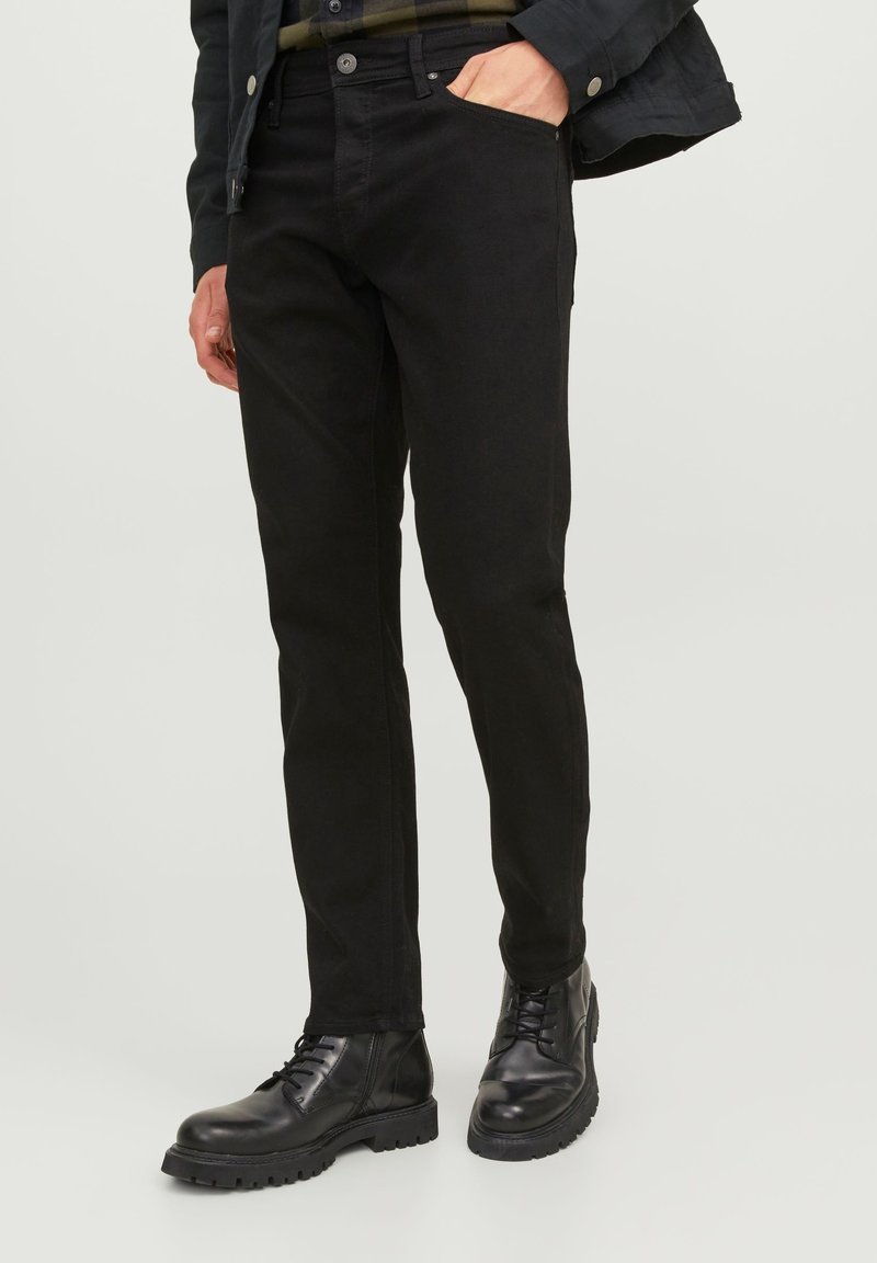Jeans negros de corte ajustado, fabricados con un denim resistente. Presentan bolsillos laterales, presillas para cinturón y una textura suave. Combinados con botas negras de cordones.
