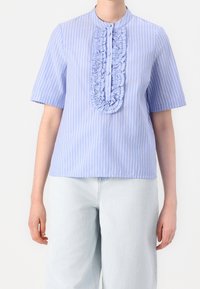 Blouse rayée bleu clair à manches courtes, avec une patte de boutonnage froncée à l'avant et une fermeture à boutons délicats. Texture du tissu lisse.