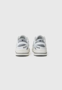 Baskets New Balance 1000 blanches et grises avec des panneaux en mesh, des cols rembourrés et une semelle intermédiaire crème avec une rayure noire.