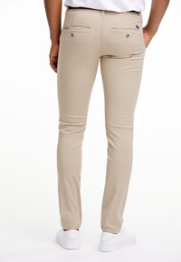 Béžové slim-fit kalhoty vyrobené z elastického materiálu, s klasickým pasem, dvěma zadními kapsami na knoflíky a rovnými nohavicemi.