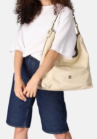 Crèmekleurige leren hobo tas met een gladde textuur, zwarte bies, zilverkleurige hardware en een geperst logo. Brede schouderriem voor comfortabel dragen.