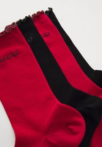 Tres pares de calcetines de canalé en colores rojo y negro alternos, con un ribete festoneado en la parte superior y un pequeño logotipo impreso cerca del puño.