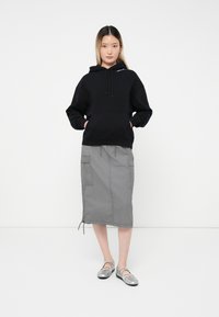 Zwarte hoodie met een voorzak, gecombineerd met een grijze midi-rok met zijzakken en een verstelbare trekkoord onderrand. Zilveren schoenen.
