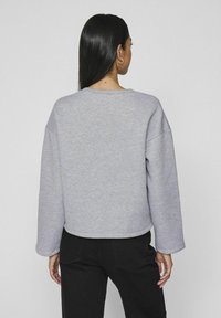 Sudadera gris de corte relajado, con hombros caídos y cuello redondeado. Tejido suave con una textura lisa, de longitud corta.