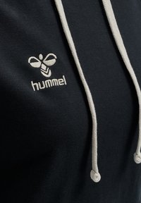 Felpa nera con cappuccio e lacci beige, con logo di ape ricamato e testo "hummel" sotto, sul davanti. Tessuto di cotone liscio.