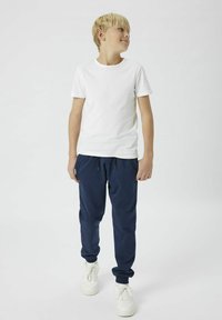 T-shirt blanc à manches courtes associé à un pantalon de jogging bleu marine et des baskets blanches. La tenue présente un design décontracté et relax avec des poignets élastiques.