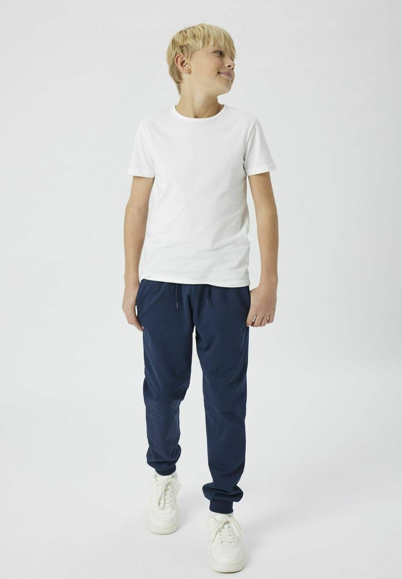 T-shirt blanc à manches courtes associé à un pantalon de jogging bleu marine et des baskets blanches. La tenue présente un design décontracté et relax avec des poignets élastiques.