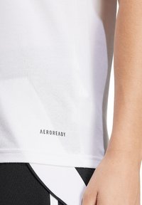 Witte sportshirt van een tekstiele, ademende stof; voorzien van "AEROREADY" branding aan de onderkant en een gestroomlijnd ontwerp.