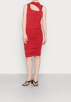 Frau trägt ein ärmelloses rotes Kleid mit gerafftem Stoff, asymmetrischem Ausschnitt und schwarzen Sandalen mit Absatz.