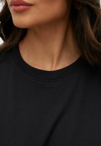 Schwarzes Baumwoll-T-Shirt mit Rundhalsausschnitt, mit glatter Textur und minimalen Nähten, aus dem Bereich des Halses gezeigt.