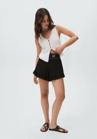 White ribbed knit top with a v-neck and three button details, paired with black ruffled hem shorts featuring a decorative belt.