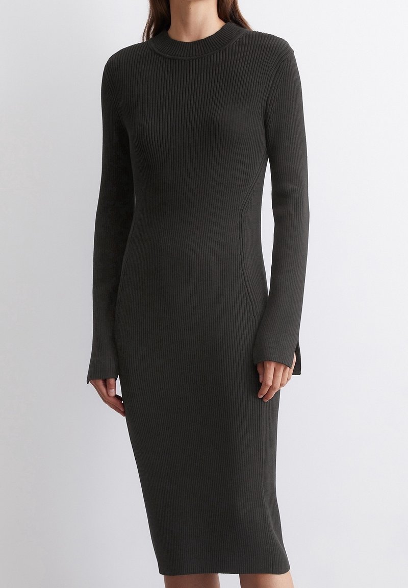 Femme portant une robe midi ajustée, manches longues, en tricot côtelé gris foncé, avec un col rond et des fentes sur les côtés à l'ourlet et aux poignets.