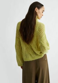 Maglione in maglia verde lime con motivo a treccia, vestibilità rilassata e orlo a costine. Indossato con pantaloni beige larghi, visto da dietro.