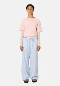 Lichtroze, cropped, fluffy trui met korte mouwen, gecombineerd met losse, lichtblauwe gestreepte broek en platte zwarte schoenen.