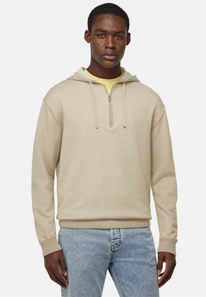 Beige Kapuzenpullover aus strukturiertem Stoff, mit einem Viertelreißverschluss vorne, gerippten Bündchen und Saum. Darunter ein gelbes Shirt getragen.