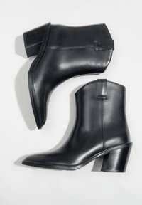 Czarne skórzane botki na kostkę z blokowym obcasem i uchwytami, przedstawione z boku i od góry na jasnym tle.