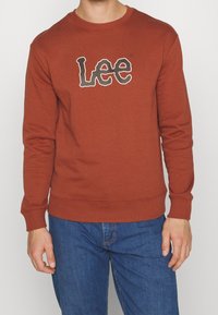 Sweatshirt v rezavé barvě s kulatým výstřihem, žebrovanými manžetami a lemem, s výrazným bílým logem "Lee" na přední straně.