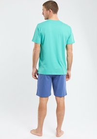 T-shirt teal à manches courtes et shorts bleu marine. Le T-shirt a un col rond ; les shorts sont de longueur genou avec une taille élastique.