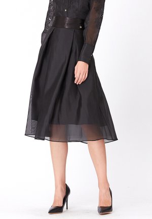 Jupe midi noire en chiffon superposé avec une taille cintrée en satin, présentant des plis et un ourlet transparent. Associée à des chaussures noires à talons hauts.