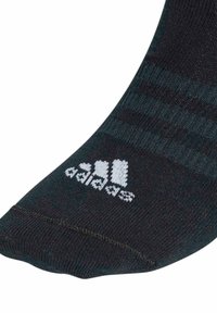 Svart idrottssocka med mörkgröna ränder och vit Adidas-logotyp. Tillverkad av texturerat material och har en avsmalnande design för en snug passform.