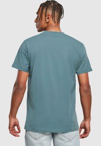 Teal värvi puuvillane T-särk lühikeste varrukatega, lõdva lõikega, ümmarguse kaelusega ja sirge servaga. Minimalistlik disain, ilma nähtavate mustrite või logodeta.