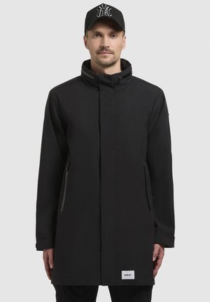 Černý dlouhý kabát s vysokým límcem, předním zipem, dvěma bočními kapsami a logem na lemu. Hladká, matná tkanina. Ležérní design.